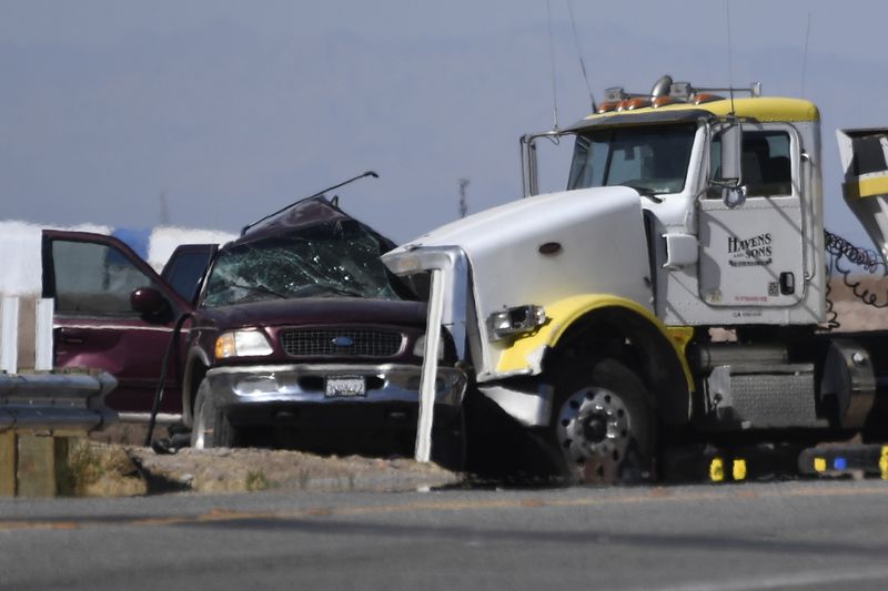 The front of a semi smashed into the driver's side of an SUV. The windshield of the SUV has shattered and the roof is bent upward.