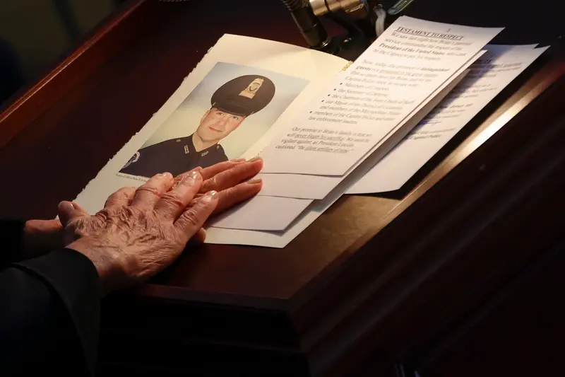 A closeup of Pelosi's hands resting on a lectern that holds Sicknick's portrait and other papers.
