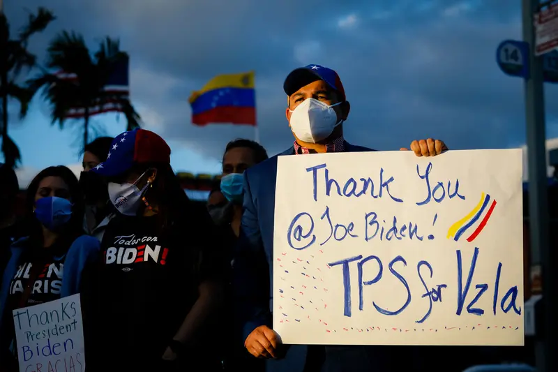 A small crowd of people wearing masks, with several holding signs. The signs say "Thank you @JoeBiden! TPS for Vzla" and "Thanks President Biden Gracias."