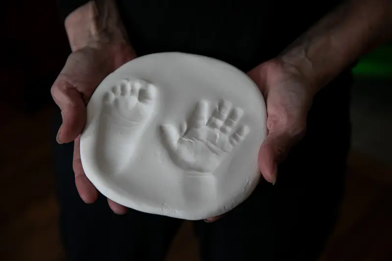 Adult hands hold a piece of plaster that has imprints of a baby's hand and foot.