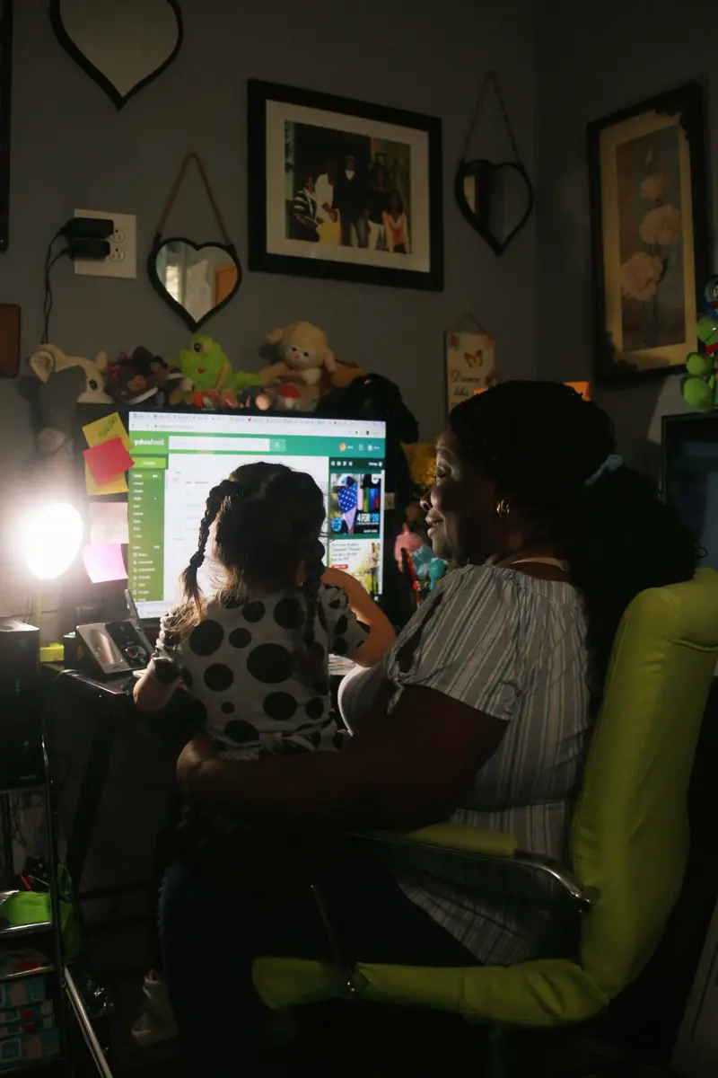 Jackie sitting in front of her computer at her desk while holding a child.