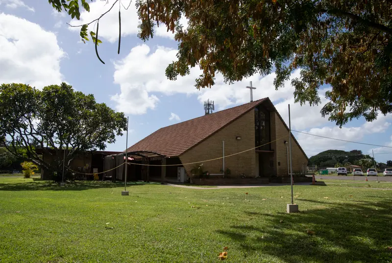 On a green lawn sits a brick building with low walls and a high, peaked roof topped by a cross.
