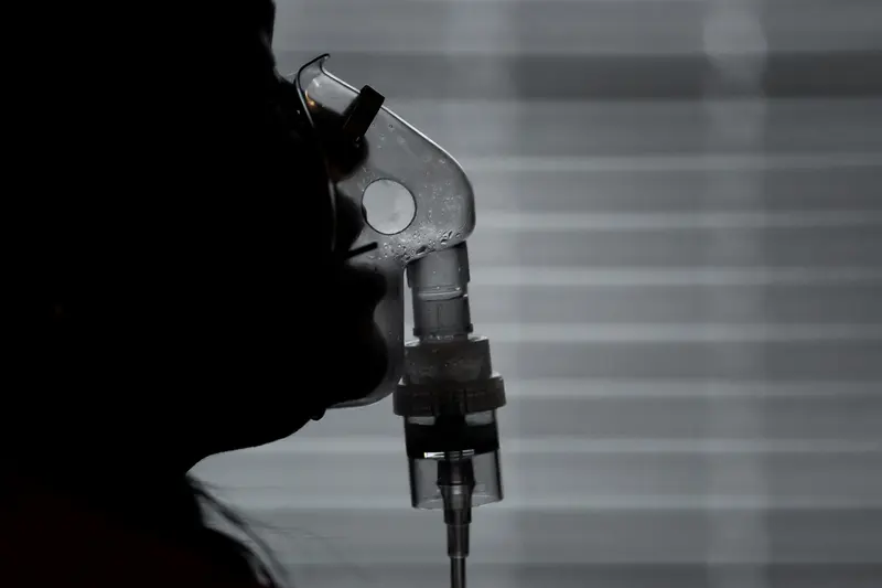 In silhouette, a mouth breathes into a clear nebulizer mask.