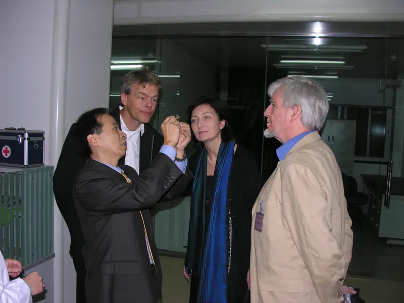 Tsien holds up a small object while three other people standing in a loose circle peer at it.