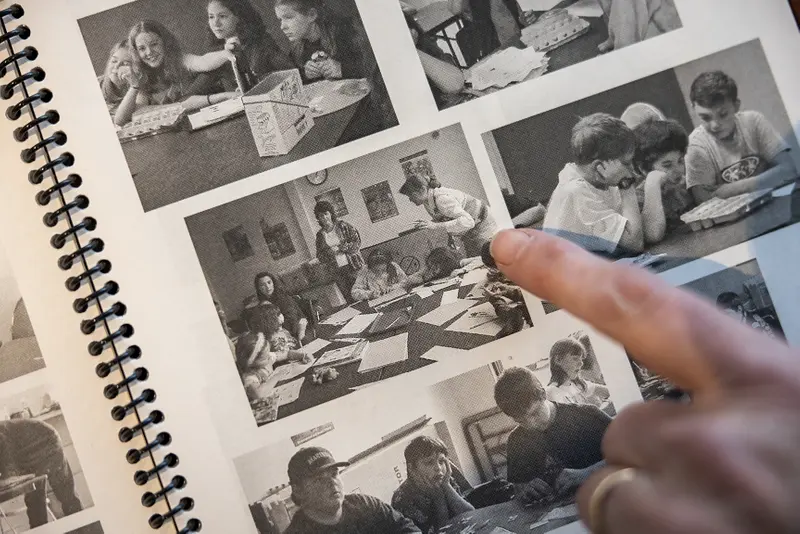 Leahy's finger points at black-and-white photos showing children doing classroom activities around large tables.