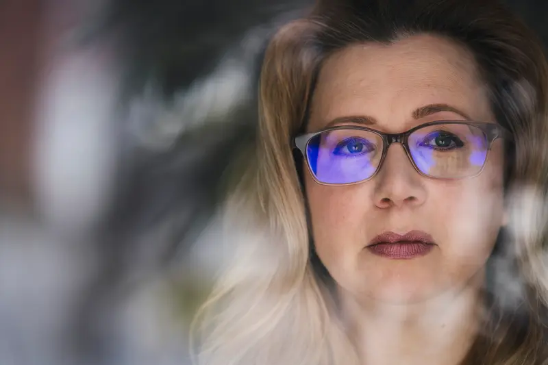 The face of a white woman with blond hair and glasses.