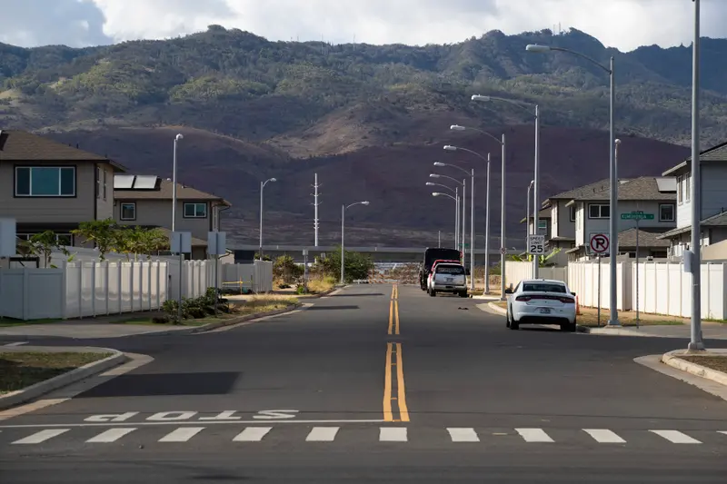 A wide suburban street of tan and white homes. Mountains rise in the background.