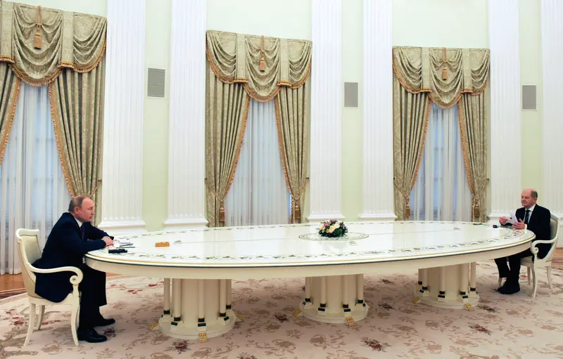 The two men sit at opposite ends of a long, white table.