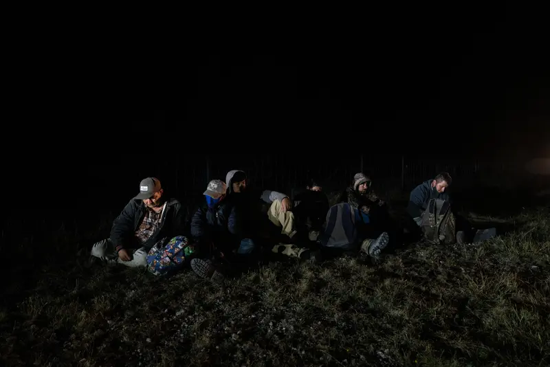 Six people sit on the grass at night, their faces mostly obscured by shadows and hat brims.