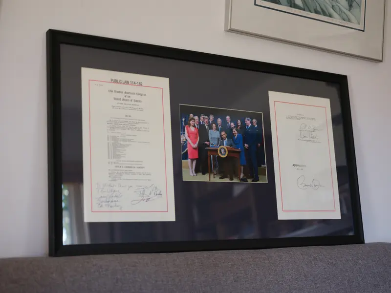 A frame holding two autographed pages of text on either side of a photo of a bill signing with President Obama.