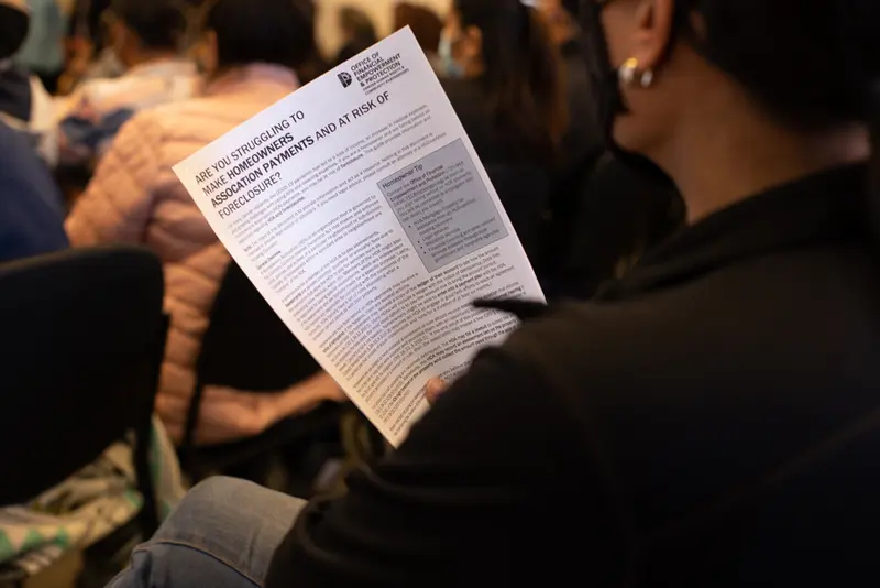 A woman holds a paper titled "Are you struggling to make homeowners association payments and at risk of foreclosure?"