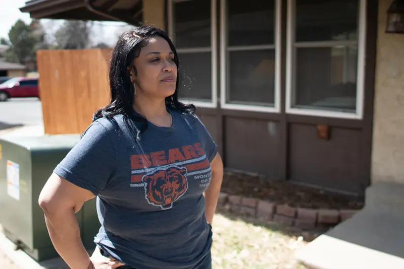 A woman in a Chicago Bears T-shirt stands in front of a tan-and-brown house.
