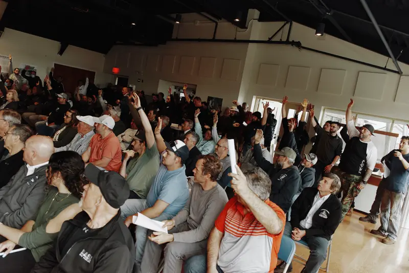 A room full of mostly men, many of whom are raising their hands.