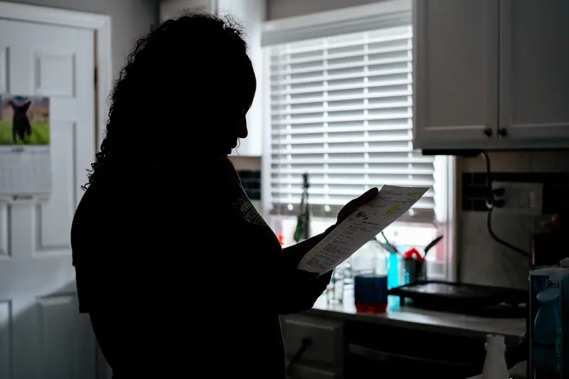 A woman, in silhouette, looks at a piece of paperwork in a kitchen.