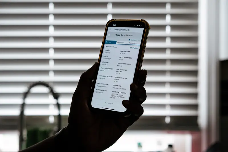 A hand holds a cellphone displaying a document reading "Wage Garnishments."