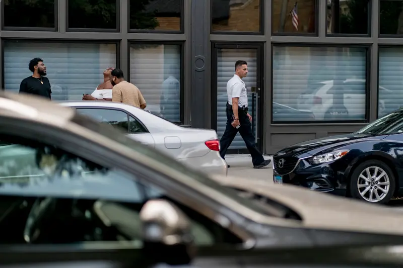 A man in a white shirt and black pants walks past a storefront with its blinds drawn.