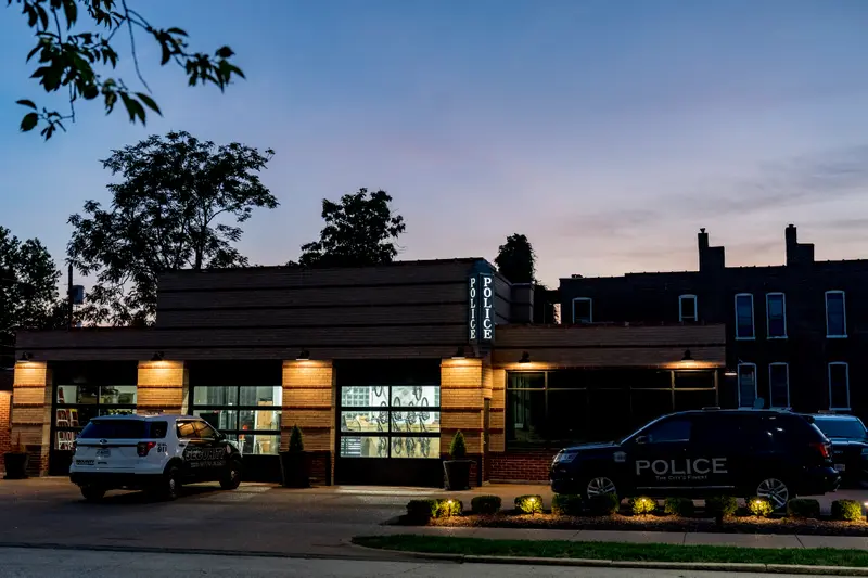 SUVs marked "POLICE" and "SECURITY" are parked outside of a building with a lit sign reading "POLICE."