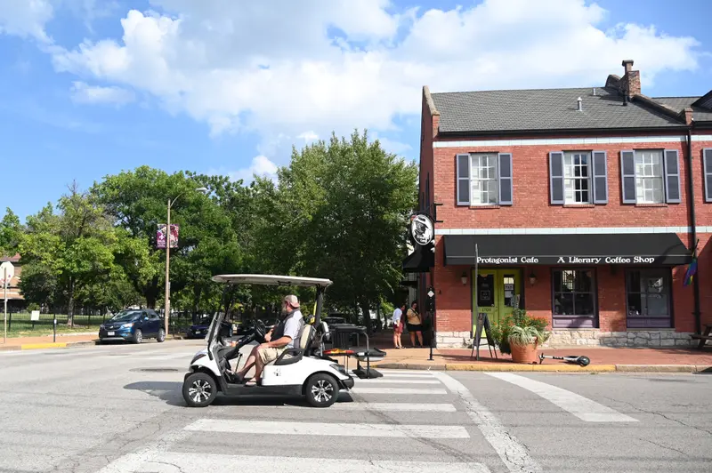 A man in a golf cart drives past a coffee shop.