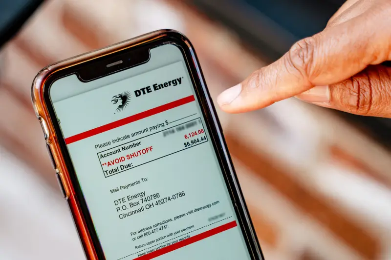 A finger points to a phone that shows the amount due to avoid shut-off is $6,124.06 and the total due is $6,904.44.