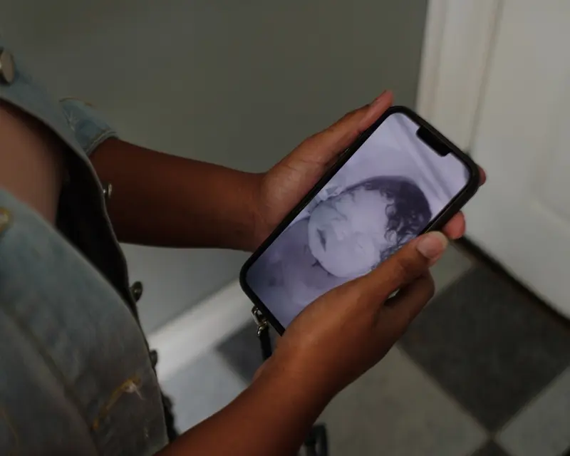 A woman's hands hold a cellphone displaying a black-and-white image of a stillborn baby.