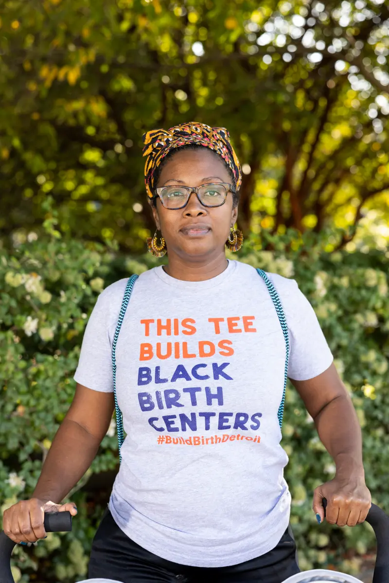 A woman in a head scarf wears a T-shirt that reads, "This Tee Builds Black Birth Centers."