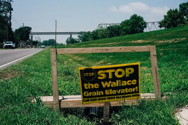 A yellow and black lawn sign beside a road reads "STOP the Wallace Grain Elevator!"