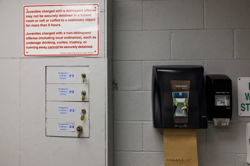 A sign with detention instructions and a set of lockers are mounted to a cinderblock wall near a paper towel dispenser.