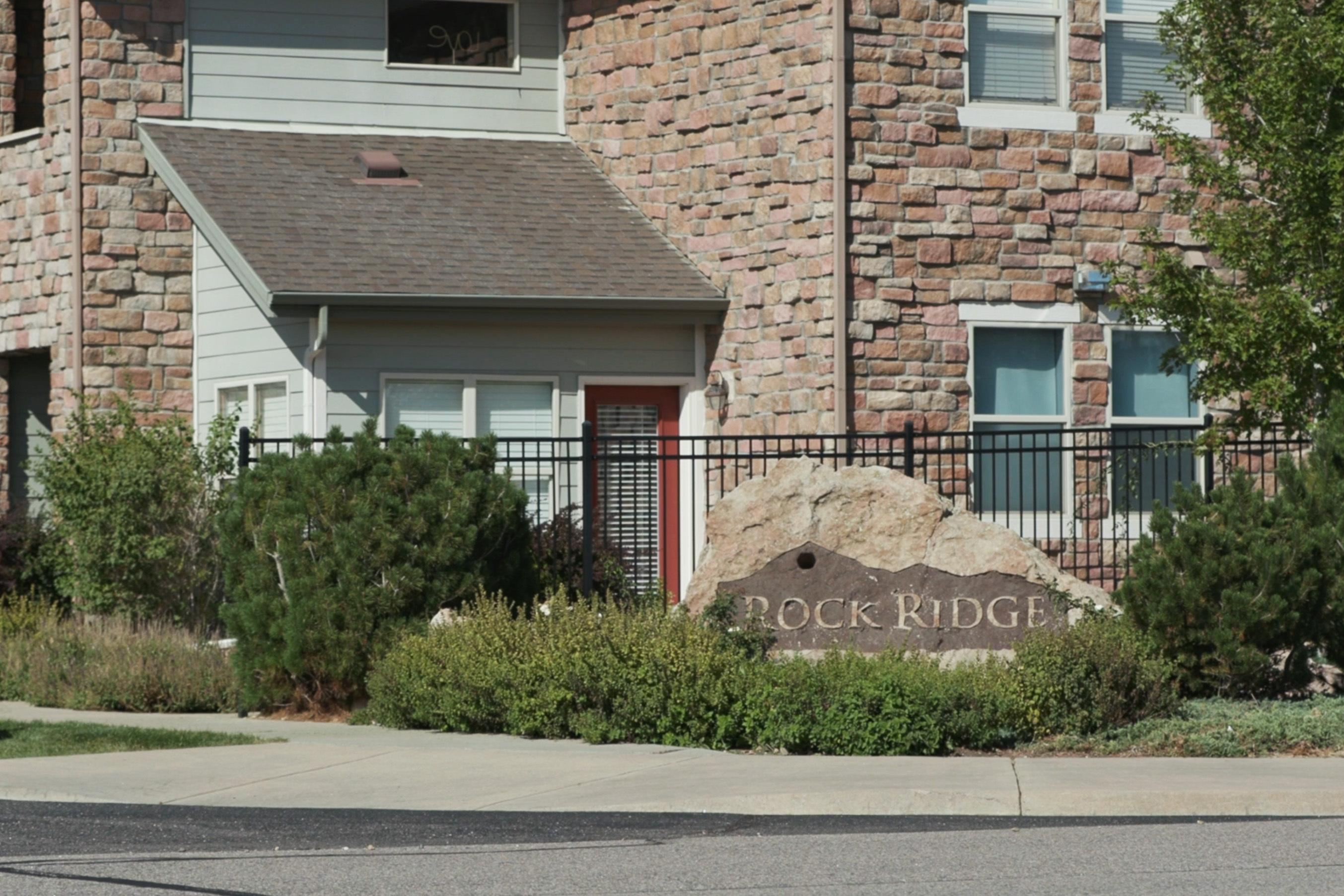 A residential building with a stone facade behind a boulder that says "Rock Ridge."