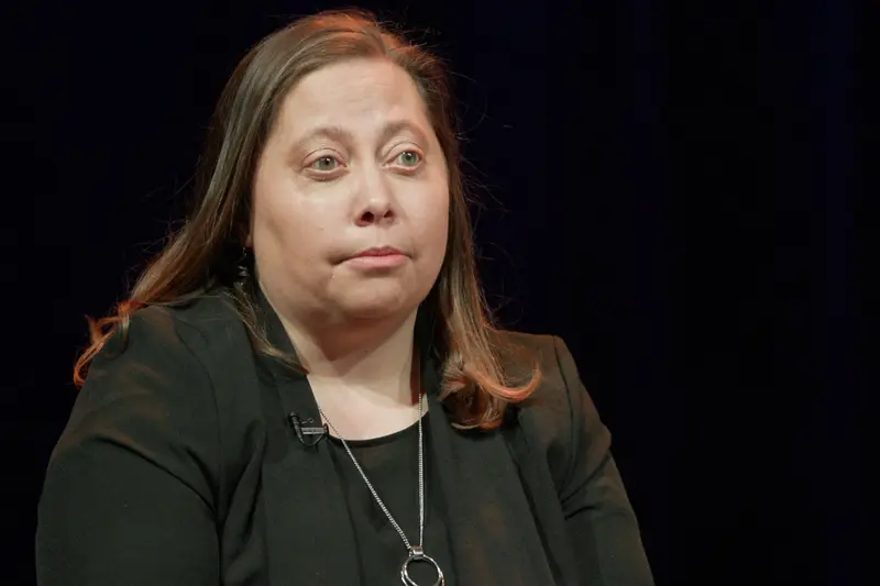 A white woman with medium-length brown hair wears a black blazer and blouse.