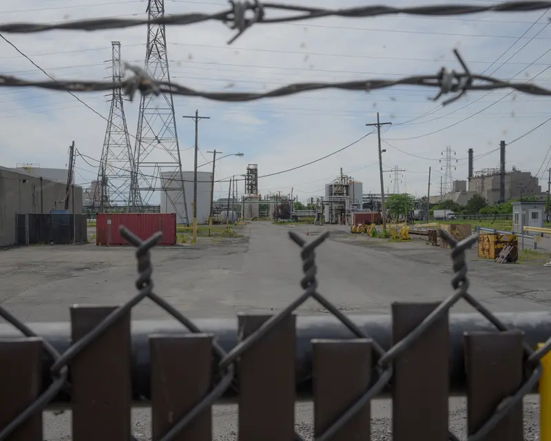 Close-up of a chain-link fence with industrial buildings beyond.