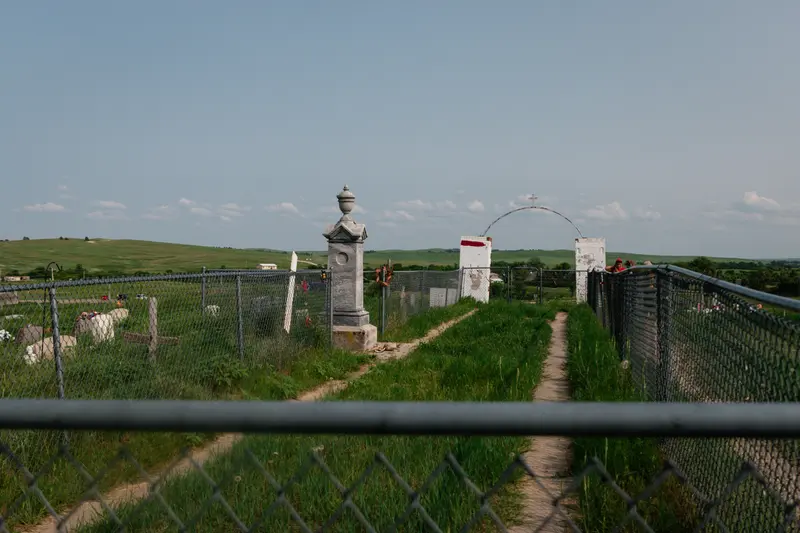 Several grave markers, surrounded by a fence, sit amidst rolling hills.
