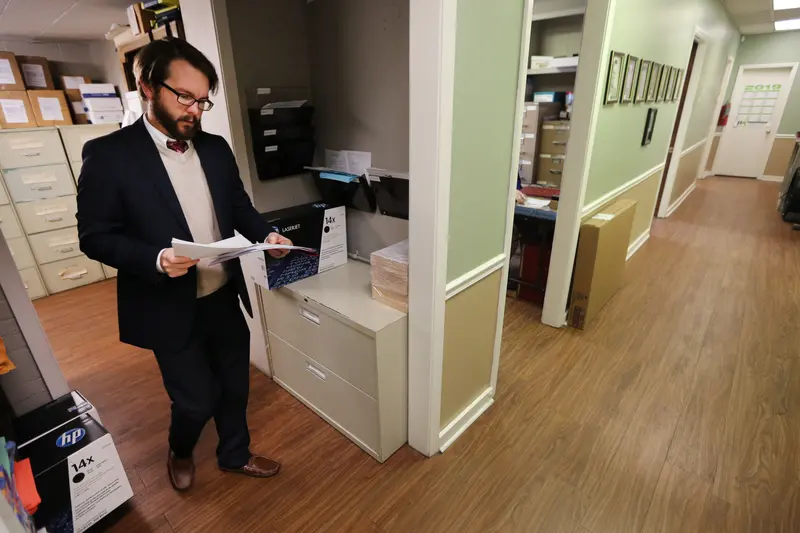A white male public defender looks at documents while walking through an office.