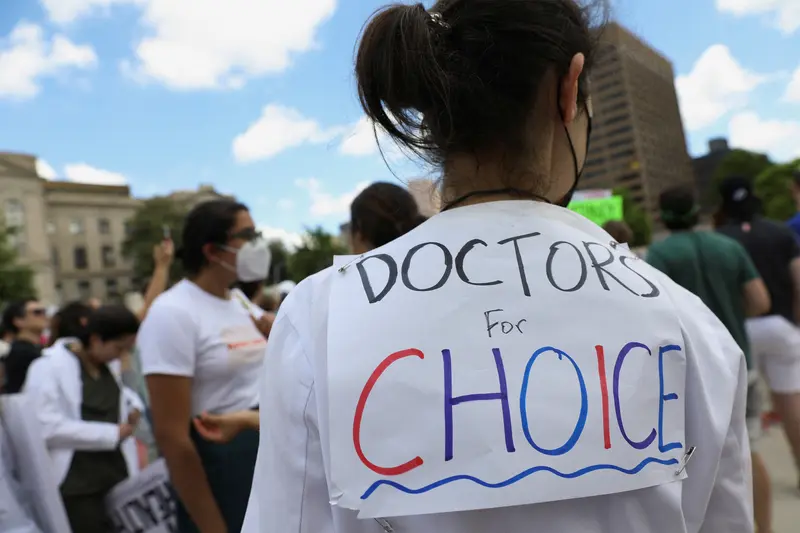 A person in a lab coat wears a "Doctors for Choice" sign on their back.