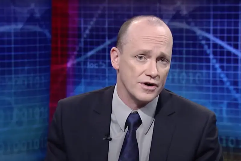 A still from a video in which a balding man in a suit is speaking.