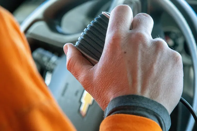 Close-up of a hand holding the microphone of a radio in a car.