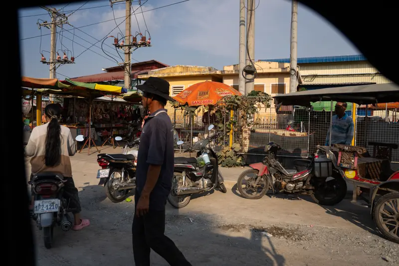 Motorcycles, people and table umbrellas are in front of one-story buildings.
