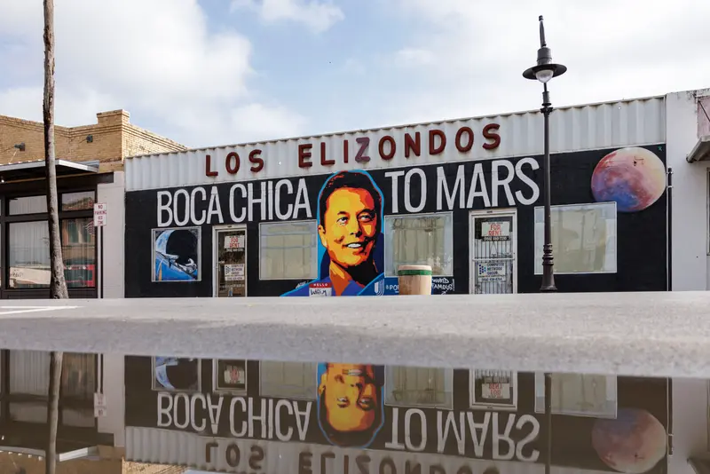 A building with a mural of Elon Musk and the phrase “Boca Chica to Mars” under a sign saying “Los Elizondos.”