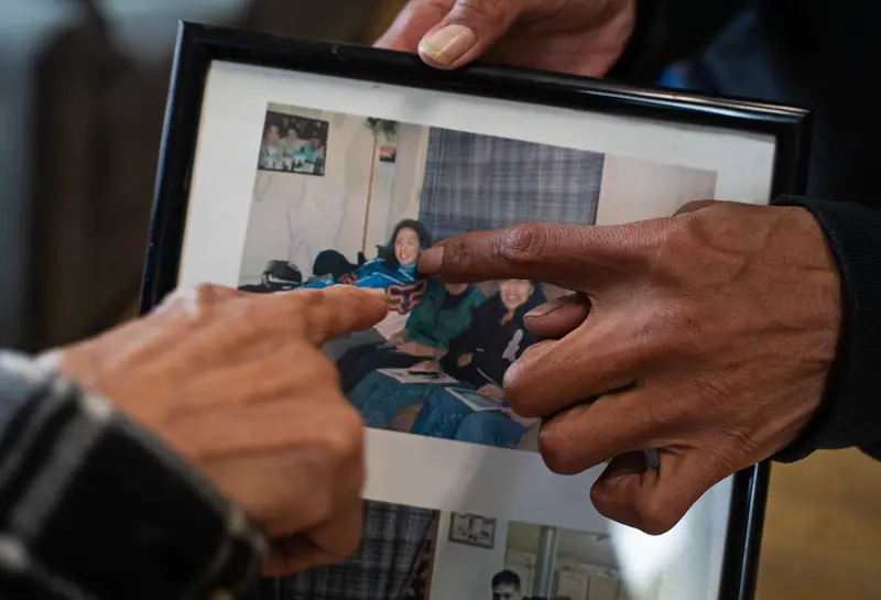 Two people's hands point to a woman in a framed photo.