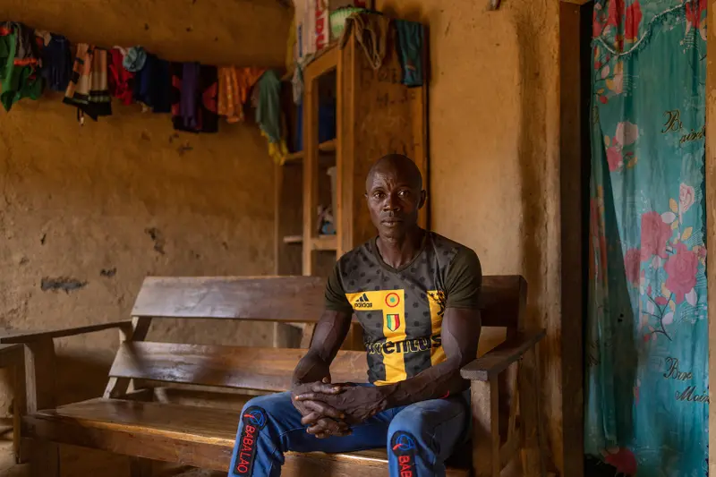 Etienne Ouamouno stares pensively into the camera in a house with orange walls and clothes hanging on a line behind him.