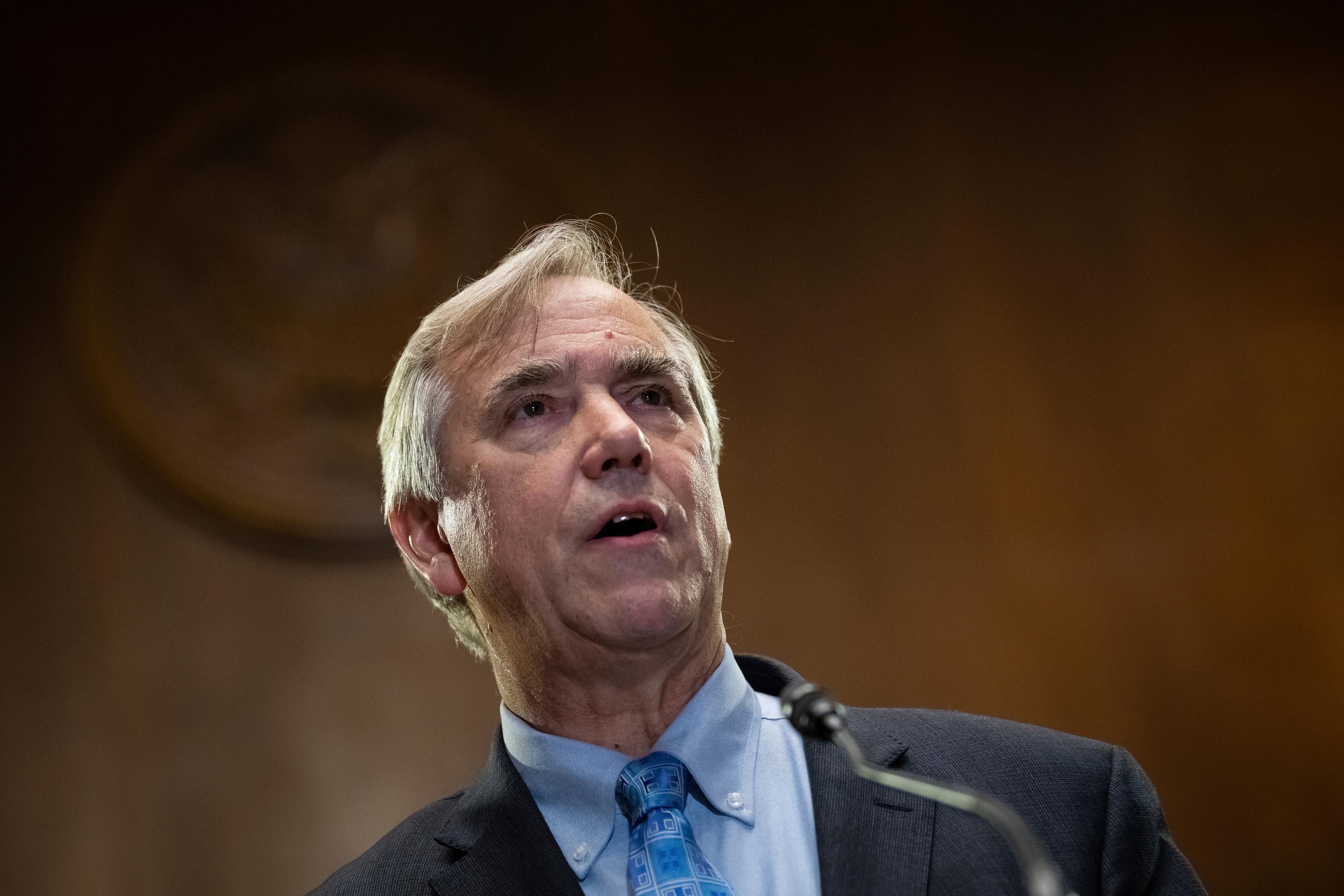 A white-haired man in a suit jacket and blue shirt and tie.