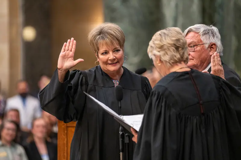 A woman in a judge's robe raises her hand to be sworn in.