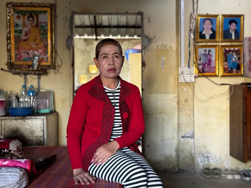 A woman wearing a red jacket over black-and-white-striped shirt and pants sits in a room with yellow walls and framed portraits.