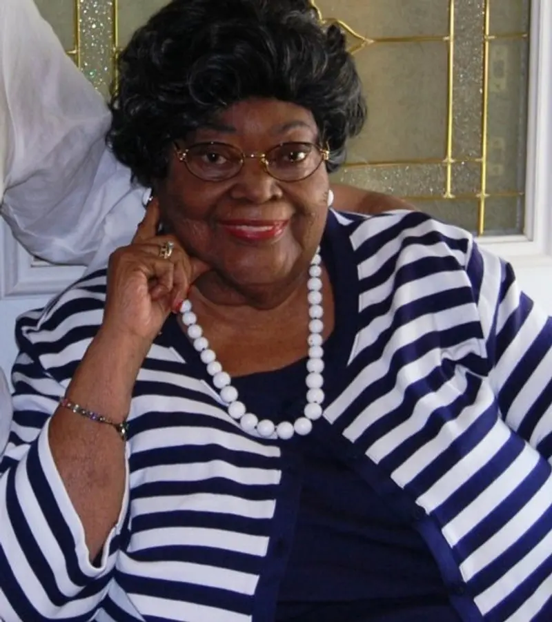 A smiling African American woman with glasses, in a striped shirt and pearls