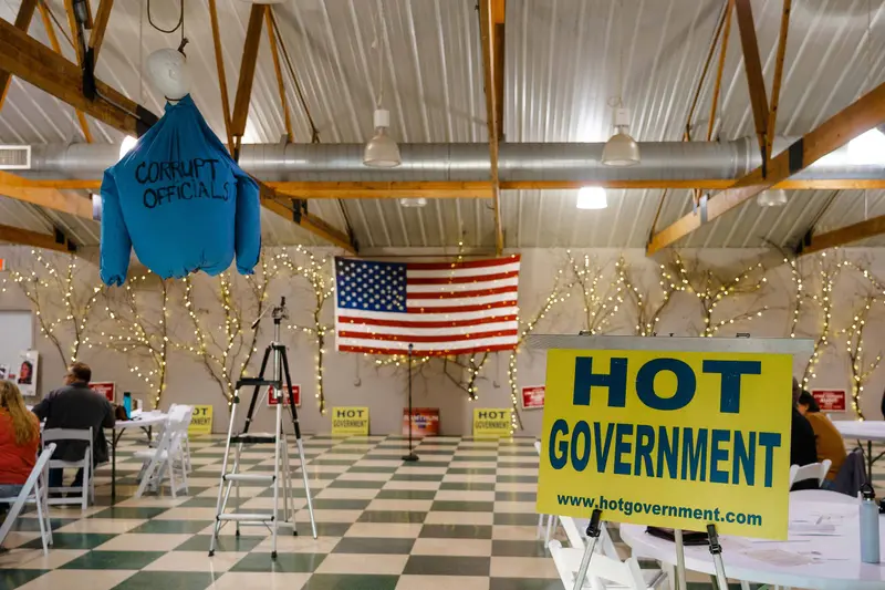 A foam torso wearing a shirt labeled "corrupt officials" hangs by the neck in a room set up with folding chairs and tables.