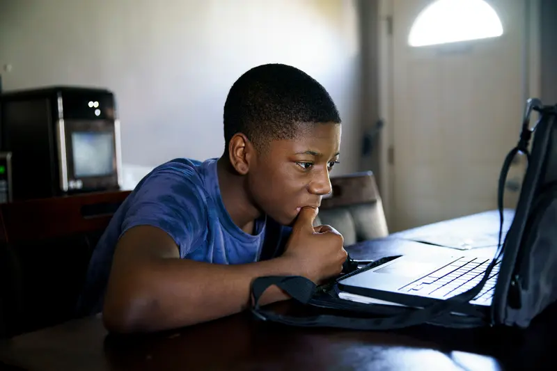 A boy stares intently at a laptop.